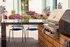 Chic outdoor kitchen featuring a modern grill and stylish seating, surrounded by vibrant flowering plants for a perfect entertaining space.