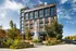 Modern urban apartment building with stylish architecture, featuring large windows and a unique outdoor art sculpture, set in a vibrant neighborhood with lush greenery.