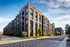 Contemporary apartment building with large windows, lush landscaping, and ample parking in a serene urban setting.