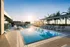 Luxurious rooftop outdoor pool area with modern sun loungers, stylish cabanas, and lush palm trees under a bright sky at sunrise.