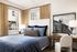 Charming bedroom with elegant decor, featuring cozy blue bedding, stylish artwork, and abundant natural light through large windows, creating a serene retreat.