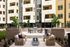 Modern apartment complex featuring a stylish outdoor seating area with cozy chairs and a central fire pit, surrounded by lush greenery.