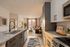 Elegant open-concept apartment with a modern kitchen, featuring granite countertops and stylish cabinetry, flowing into a cozy living room with warm natural light.