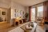 Charming living room with stylish decor, featuring warm wooden floors, elegant artwork, plush seating, and abundant natural light through large windows.