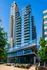 Modern glass apartment building with spacious balconies and lush greenery at the entrance. Prime location with stunning city views.