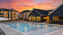 Luxury apartment complex with stunning poolside view at sunset, featuring modern building design and ambient lighting.