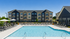 Luxurious apartment complex featuring a large pristine swimming pool, modern architecture, and relaxing lounge chairs under sun umbrellas, perfect for upscale living.