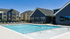 Luxurious apartment complex with a pristine swimming pool, modern lounge chairs, and stylish buildings under a bright blue sky.