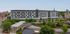 Modern urban apartment building with sleek exterior design, featuring lush greenery and convenient street-level shops, ideal for vibrant city living.
