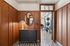 Elegant apartment entrance with wood paneling, a chic black cabinet with a marble top, and a stylish lamp, leading to a modern gym with exercise equipment.