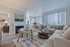 Inviting living room featuring a cozy beige sectional, stylish armchair, and chic round coffee table, flooded with natural light through large windows, creating a warm and welcoming space.