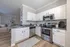 Modern kitchen with sleek white cabinets, stainless steel appliances, and an open view to a cozy, stylish living room.