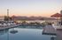 Luxurious rooftop pool with scenic mountain views and colorful artistic wall, surrounded by elegant lounge chairs and umbrellas at sunset.