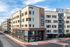 Modern apartment complex, AZUR, showcasing elegant architecture with spacious balconies and vibrant ground-level retail space, beautifully set against a bright blue sky.