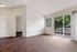 Bright and spacious room with rich wood flooring, white walls, and a large glass door leading to a charming balcony overlooking lush greenery.