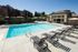 Inviting outdoor swimming pool with stylish lounge chairs and modern clubhouse backdrop, surrounded by lush greenery and serene ambiance.