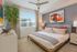 Bright, modern bedroom featuring a stylish bed with striped pillows, vibrant artwork, and a chic ceiling fan.