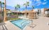 Modern apartment complex featuring a luxurious pool area with stylish lounge chairs, vibrant palm trees, and a sunlit patio.