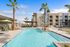 Inviting apartment complex with a pristine swimming pool, surrounded by palm trees and modern architecture under a vibrant blue sky.