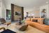 Modern living room with elegant decor, featuring a stylish tan leather sofa, geometric wooden coffee table, and vibrant abstract art on the walls.