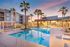 Luxurious apartment complex with a serene swimming pool area, surrounded by palm trees and modern amenities at sunset.
