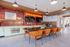 Modern communal space with stylish orange chairs, a sleek black table, and a vibrant red tiled accent wall, perfect for social gatherings.