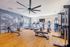 Bright and modern gym with state-of-the-art exercise equipment, including treadmills, stationary bikes, and rowing machine, under a large ceiling fan and stylish wall art.