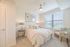 Bright and airy bedroom with elegant decor; features a cozy bed, chic nightstands with stylish lamps, and a large window letting in natural light.