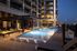 Luxurious apartment complex with a stunning rooftop pool, elegant outdoor seating, and illuminated windows showcasing modern living spaces at dusk.