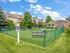 Bark Park fenced in with green grass and some obstacles the animals can use. Green trees surrounding the area with a gazebo in front of the building.