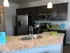 Granite speckled counter top with a chrome singular sink and silver appliances like, fridge, microwave and over/stove. Dark brown cabinetry with two hanging lights from the ceiling
