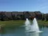 Large pond with two fountains in the middle surrounded by two story apartments with green grass and trees around the water