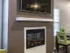 Fireplace on a light brown wall below a flat screen TV. A dining room table with a modern green chair next to it