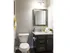 Bathroom view white porcelain toilet with a singular sink with dark cabinets and granite counter top. Two lights above the mirror