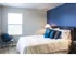 Bedroom split with dark blue and light grey paint. Large bed in the middle and a corner chair across from the bed. Light grey carpet
