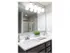 Side view of bathroom with double sinks in between there is a white box holding a layer of green grass decorative. White counter tops with chrome sinks