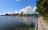 Curving lakeside path with black railing, tree shade, and expansive water views under a blue sky.