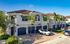 Charming Mediterranean-style townhomes with tile roofs, palm trees, and attached garages under a bright blue sky.