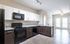 Modern kitchen with sleek dark cabinets, granite countertops, and stainless steel appliances, leading to a bright, open-concept living area.