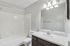 Modern and bright bathroom featuring sleek fixtures, a pristine bathtub, and a spacious vanity mirror, perfect for relaxation.