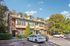 Charming townhouse exterior surrounded by lush greenery, featuring modern architecture with dormer windows and ample parking space.