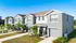 Charming townhouses with modern gray exteriors, manicured lawns, and lush greenery, set under a clear blue sky.