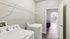 Modern laundry room with sleek white washer and dryer, featuring open shelving and view into sunlit living area with large window.