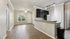 Bright modern apartment interior with open-plan layout, featuring elegant wood flooring, a sleek kitchen with dark cabinets and granite countertops, and a sunlit living area with a large arched window.