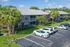Charming two-story apartment complex surrounded by lush greenery and palm trees, featuring ample parking and modern design.
