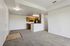 Modern open-concept living area with plush carpet and a sleek kitchen featuring wooden cabinetry and granite countertops.