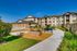 Charming apartment exterior with lush greenery, vibrant community garden, and inviting benches under a clear blue sky.