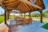 Charming outdoor pavilion with rustic wooden beams and inviting dining area surrounded by lush greenery, perfect for gatherings and relaxation.