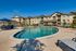 Inviting luxury apartment complex with a sparkling resort-style swimming pool, sun loungers, and landscaped garden area on a sunny day.