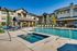 Elegant apartment complex featuring a luxurious swimming pool, hot tub, and stylish outdoor lounge area with umbrellas and seating.